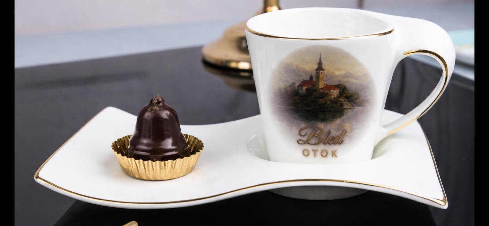A chocolate bell on a saucer next to a cup with a motif of Bled Island